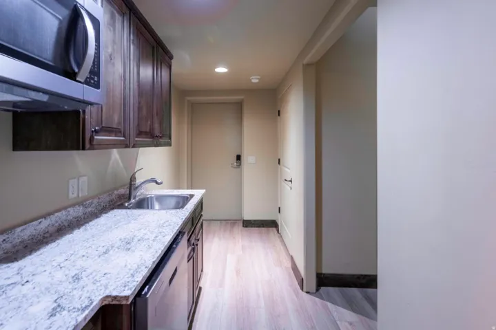 Built-in microwave, wood cabinetry, stone-finish countertop, stainless steel sink with a gooseneck faucet, and wood-finish flooring