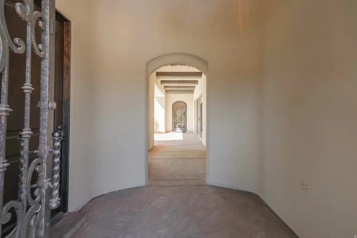 Wrought iron security door with intricate scrollwork, arched doorway, exposed wood beams, and a smooth stucco finish