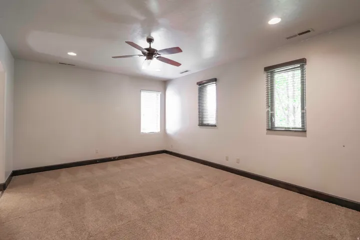 Recessed lighting, ceiling fan, three windows with horizontal blinds, neutral tone carpet, and dark wood trim