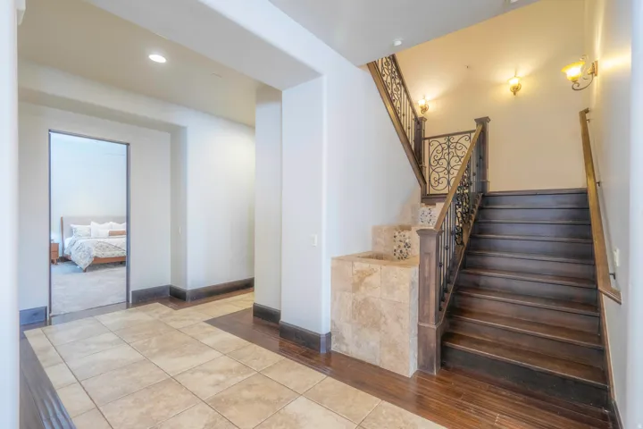 Tile flooring, dark wood-finish flooring, wood staircase with wrought iron balusters, wall sconces, recessed lighting