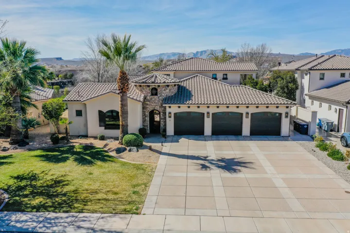 Stucco exterior with stone accents and arched entry, three-car garage, tile roof, and a patterned concrete driveway