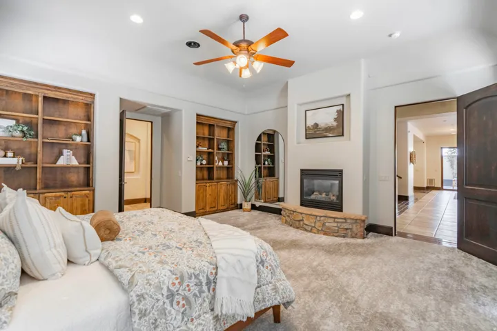 Recessed lighting, wood-finish ceiling fan, built-in shelving, stone-surround fireplace, and wood-panel doors