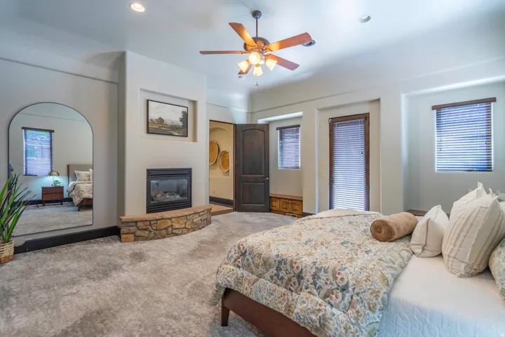 Built-in fireplace with stone surround, recessed lighting, ceiling fan, dark wood doors, and multiple windows with blinds