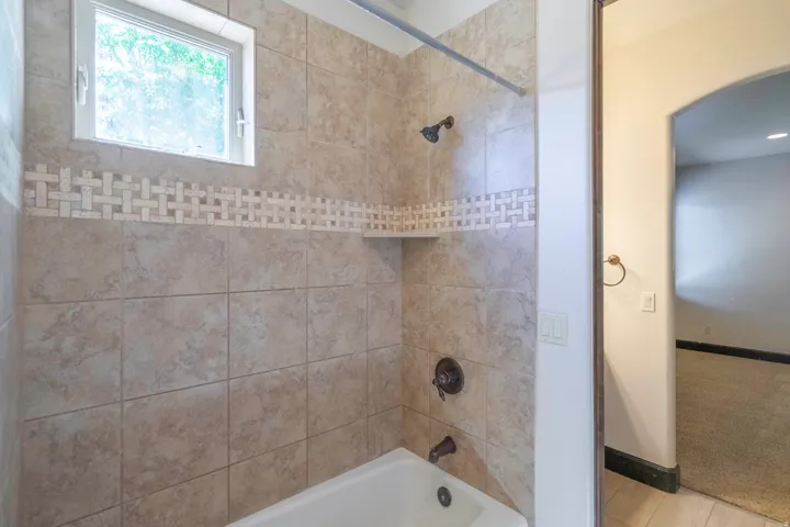 Bathtub with tile surround, decorative tile accent band, built-in shower shelf, and bronze-finish fixtures