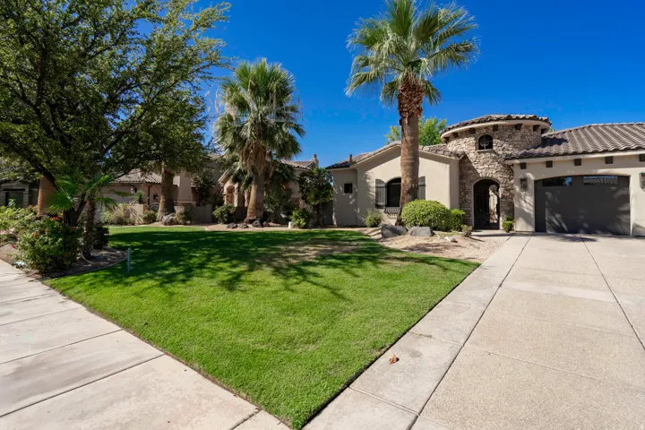 Stucco exterior with stone accents, concrete tile roof, attached garage, and mature palm trees