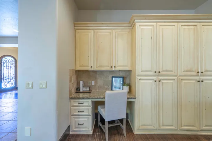 Built-in desk with stone-finish countertop, coordinating tile backsplash, and ample cabinetry
