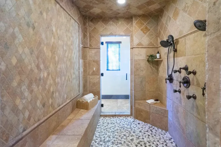 Walk-in shower with pebble tile flooring, dual shower heads, and built-in bench seating
