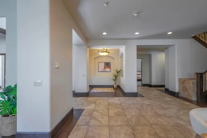 Large format floor tile, recessed lighting, arched entryway, dark wood-finish flooring, wrought iron staircase railing