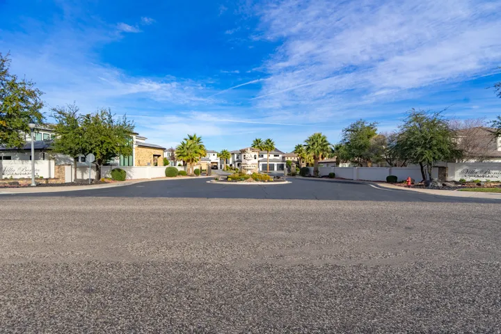 Community entrance featuring a central roundabout, mature trees, and established landscaping