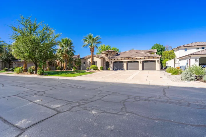 Stucco exterior with stone accents, a three-car garage, a tiled roof, and a paved driveway
