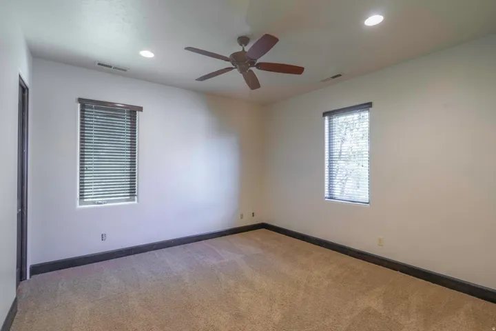 Recessed lighting, ceiling fan, two windows with blinds, and neutral carpeting