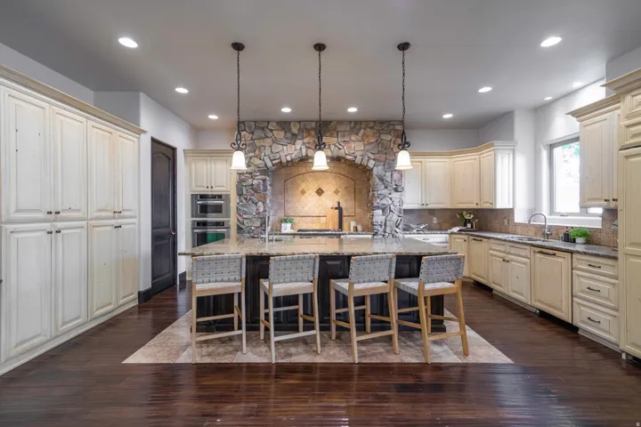 Spacious kitchen featuring an expansive center island, integrated stone archway with backsplash, built-in double ovens, extensive cabinetry, and recessed lighting