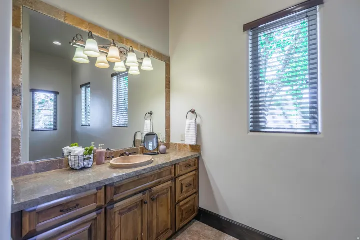 Wood-finish vanity with multiple storage cabinets and drawers, stone countertop, integrated basin, and a large mirror framed with stone-finish material