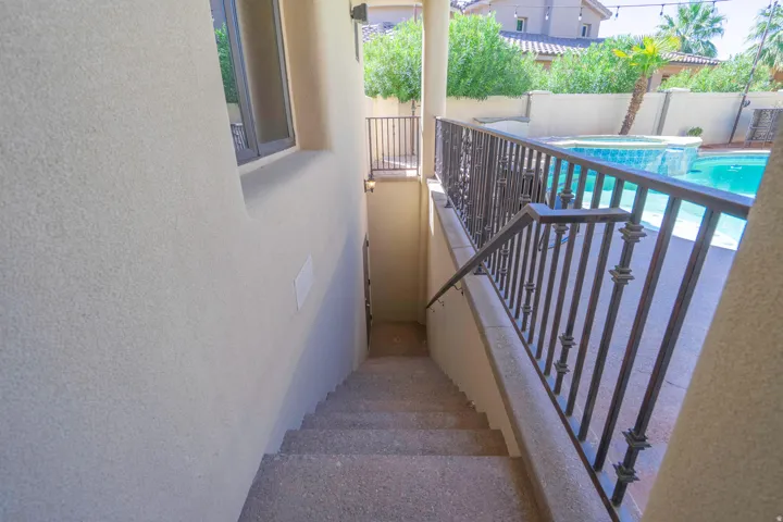 Stucco exterior with a window, wrought iron railings, and concrete stairs leading to a pool area with a spa