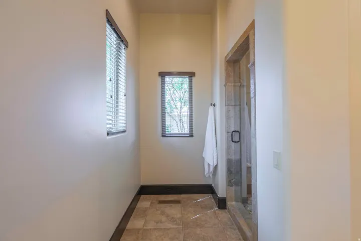 Tiled flooring, dual windows with blinds, and a glass-enclosed shower with a dark-framed door