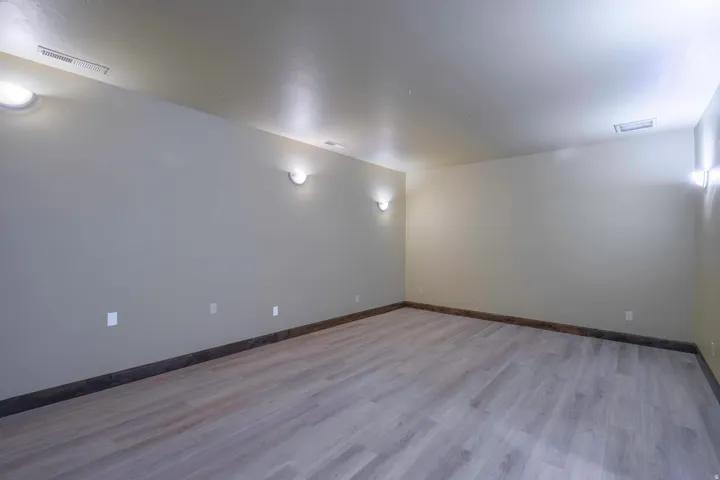 Spacious room featuring wood-finish flooring, neutral-toned walls, and multiple wall-mounted light fixtures