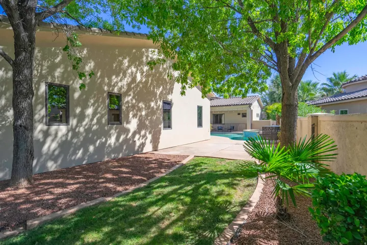 Stucco exterior with multiple windows, mature trees, manicured lawn, and a paved patio area with a visible pool