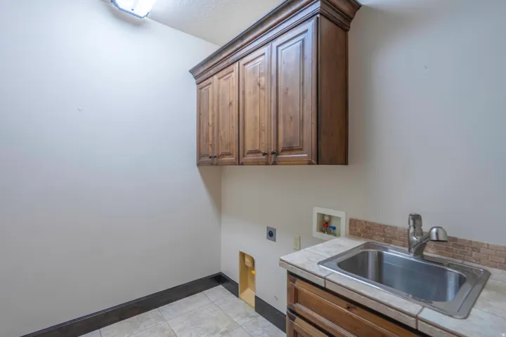 Wood cabinetry with crown molding, stainless steel sink, tiled countertop, and tiled flooring