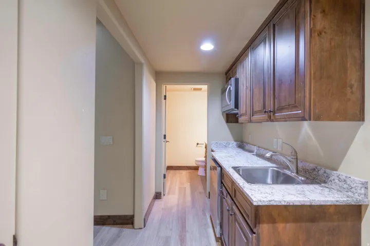 Compact kitchenette with wood cabinetry, stainless steel sink, and light-toned countertop