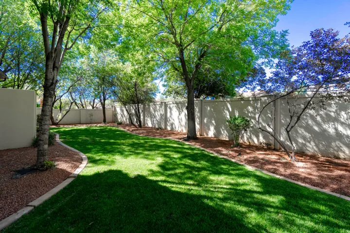 Expansive lawn bordered by mature trees and a privacy wall