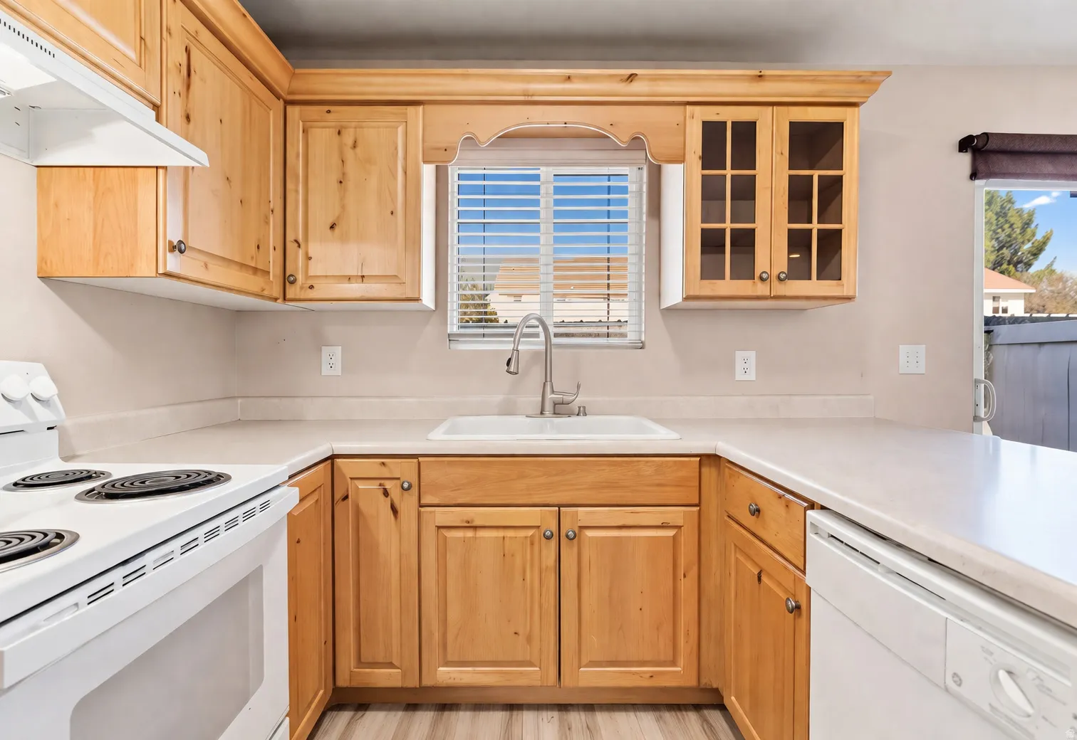Wood-finish cabinetry, white countertop, white range, built-in dishwasher, and a stainless steel faucet