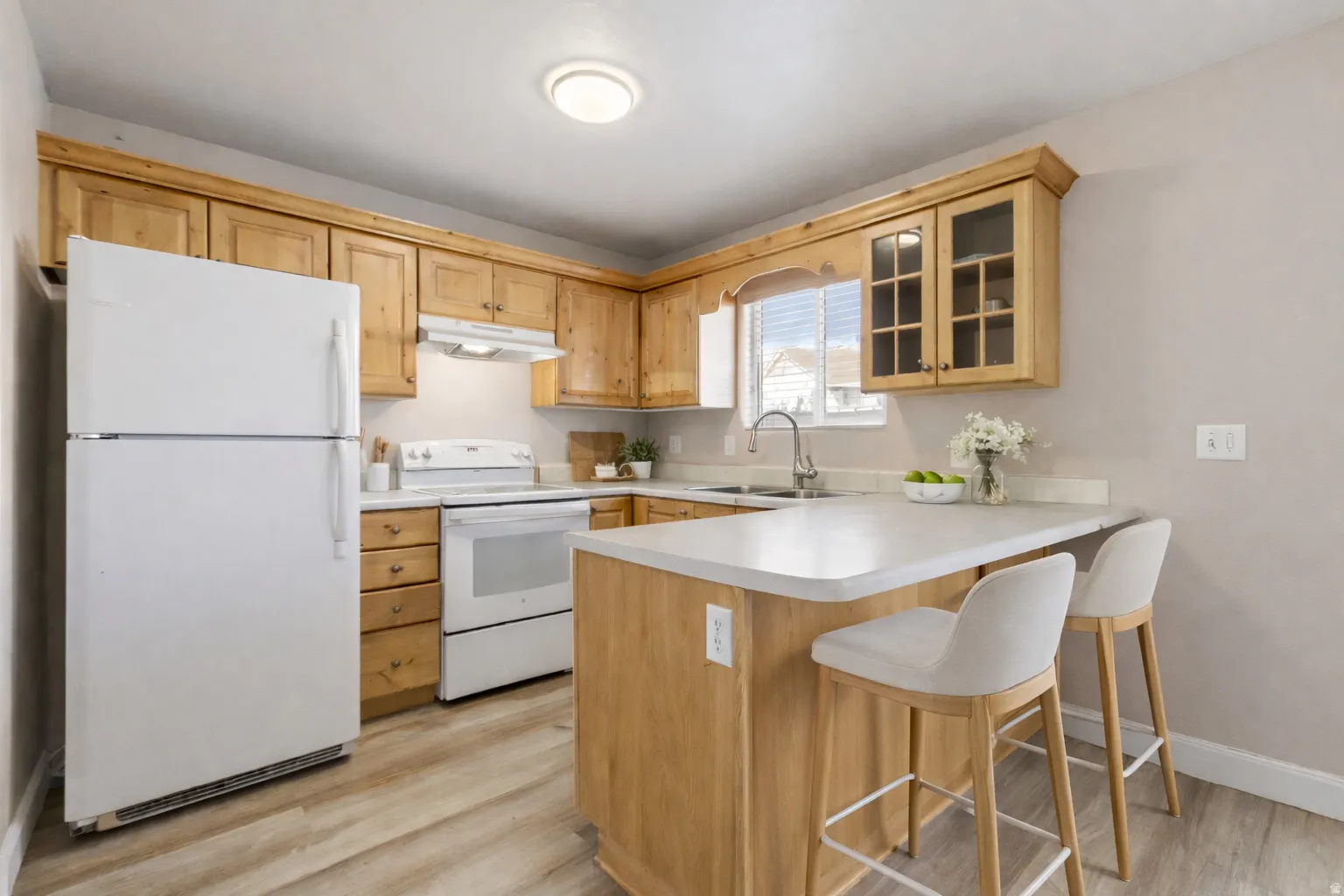 Kitchen featuring wood cabinetry, white appliances, a peninsula with an extended countertop, and wood-finish flooring