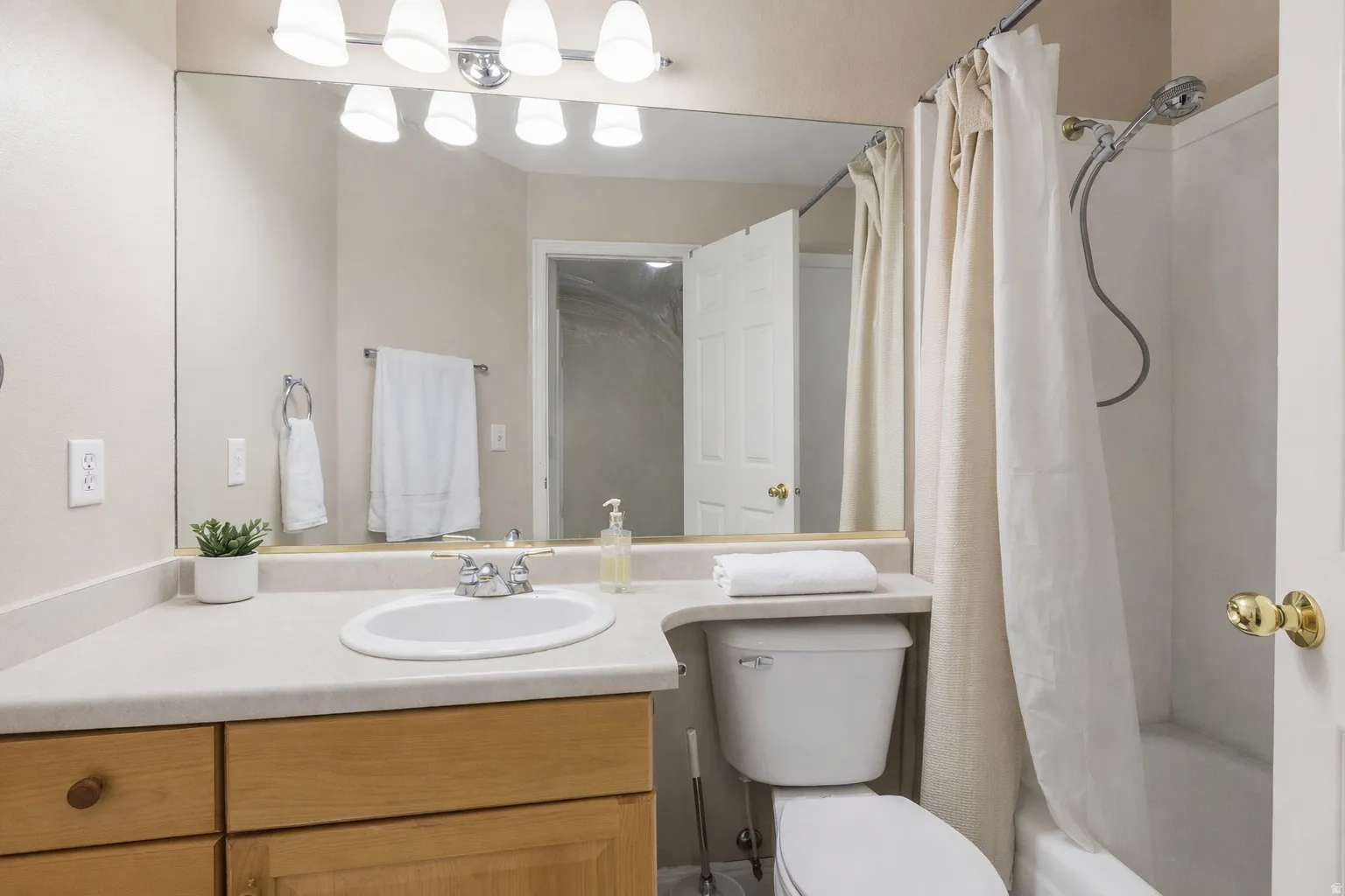 Bathroom featuring a light-toned vanity with an integrated sink, a large wall-mounted mirror, and a shower-over-tub combination
