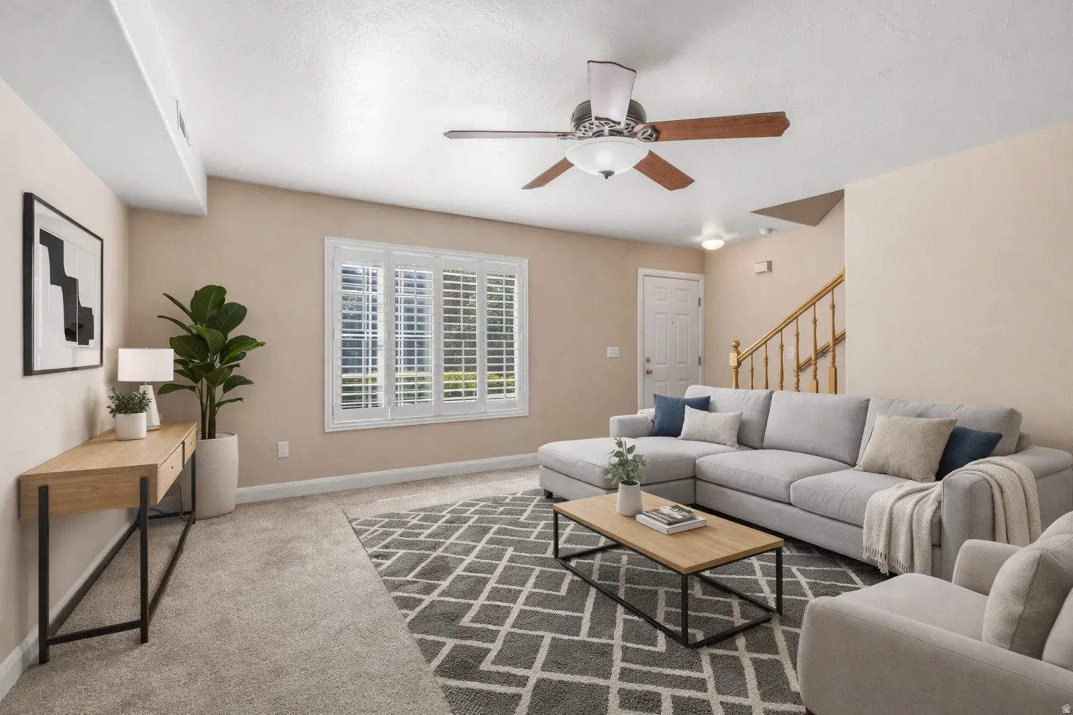 Plush carpet flooring, white window shutters, ceiling fan with integrated lighting, wood-finish staircase railing, and a white paneled door