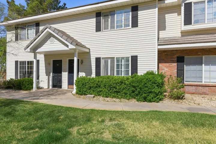 Exterior featuring horizontal vinyl siding, a covered entry with columns, black louvered shutters, and brick accents