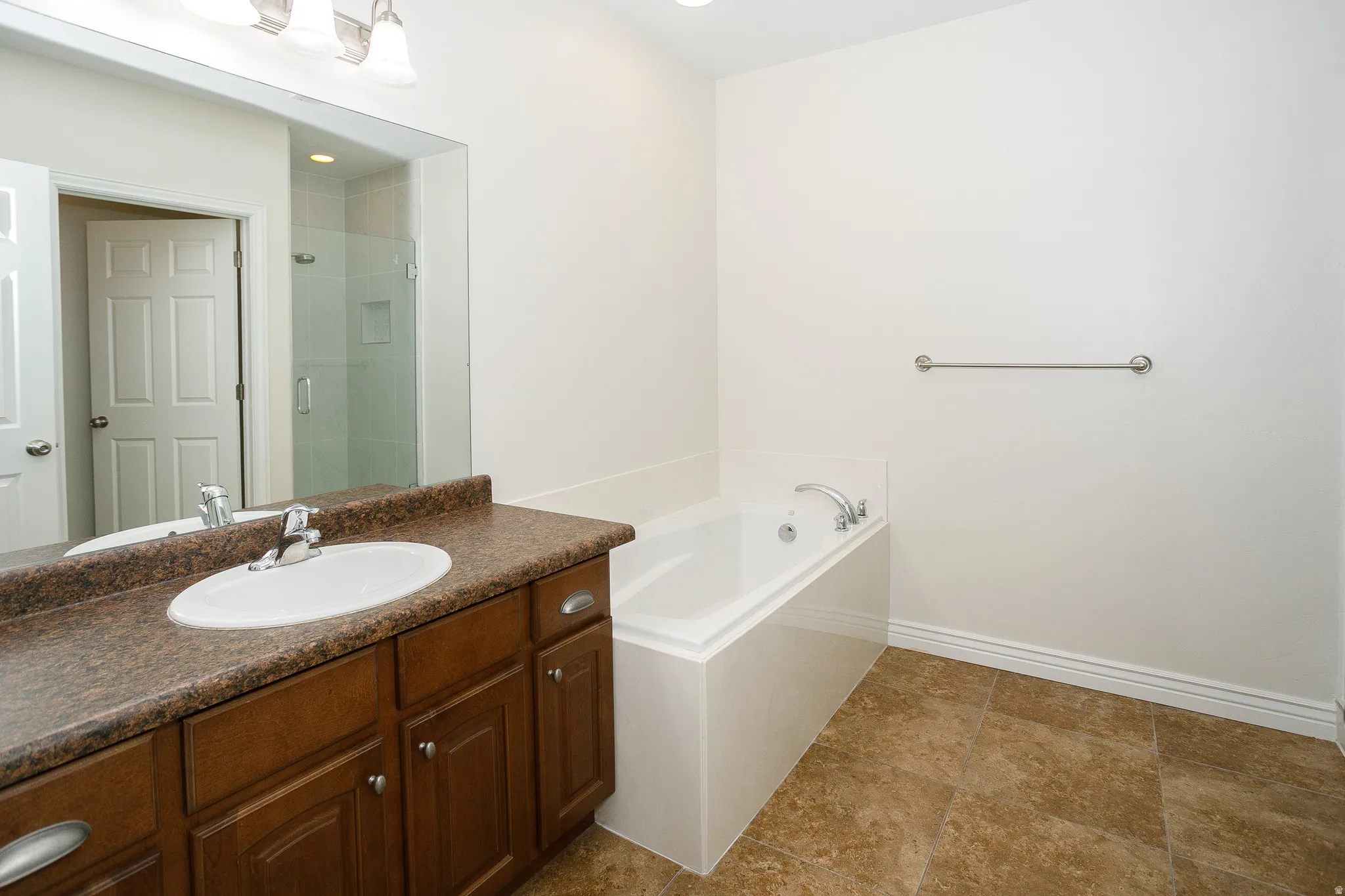 Spacious bathroom featuring a built-in soaking tub, a vanity with a drop-in sink, a large wall-mounted mirror, and tile flooring