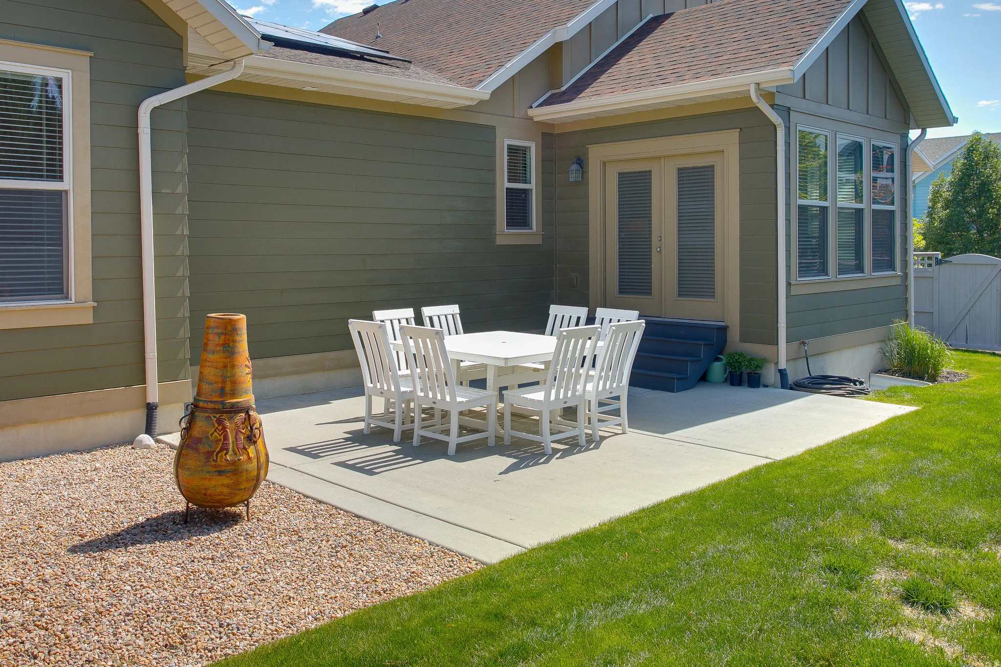 Expansive concrete patio with French doors, surrounded by a manicured lawn and gravel hardscaping
