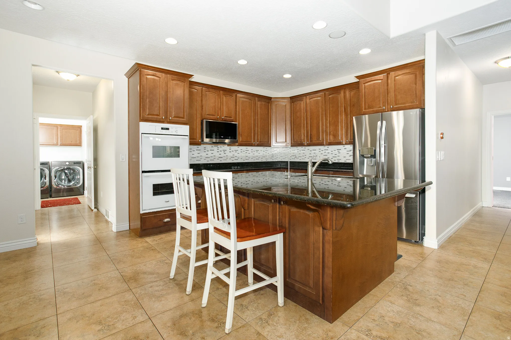 Kitchen featuring wood cabinetry, integrated double ovens, stainless steel appliances, and an island with a dark countertop