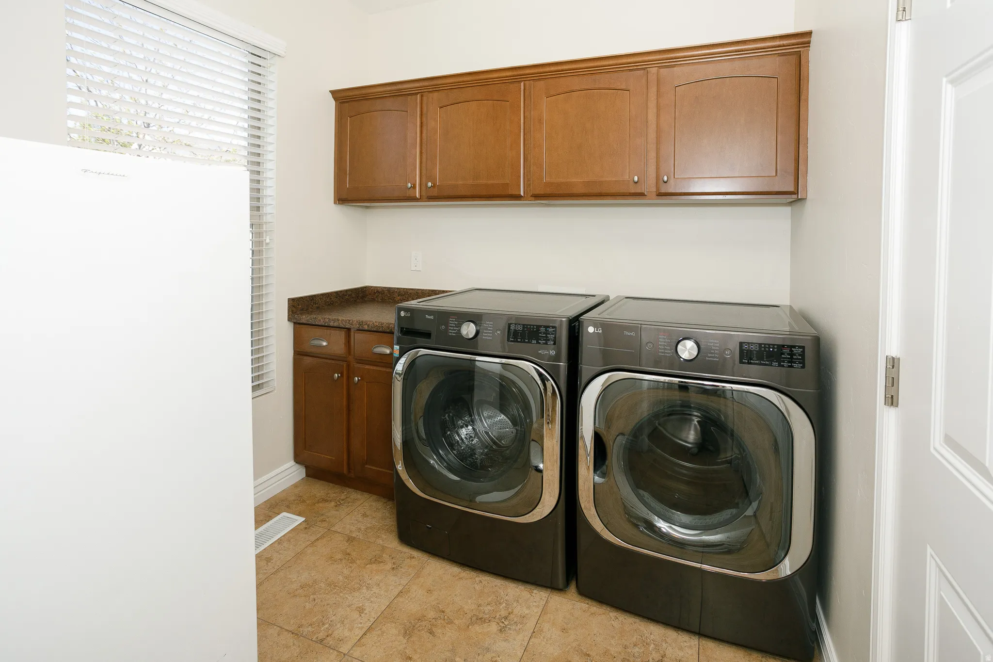 Laundry area with wood-finish cabinetry, speckled countertop, and tiled flooring