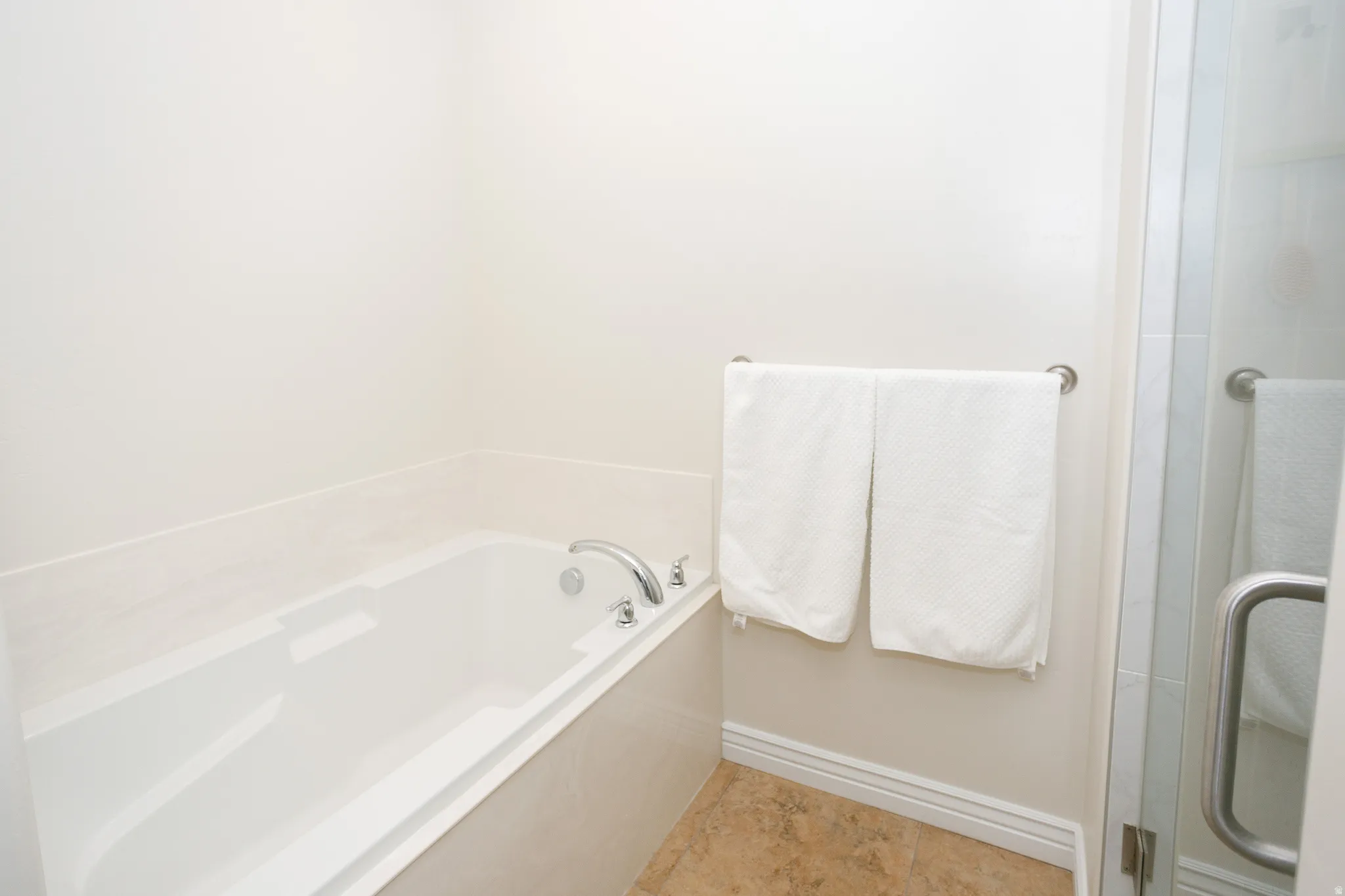 Soaking tub with chrome fixtures and surrounding tile, complemented by a glass-enclosed shower