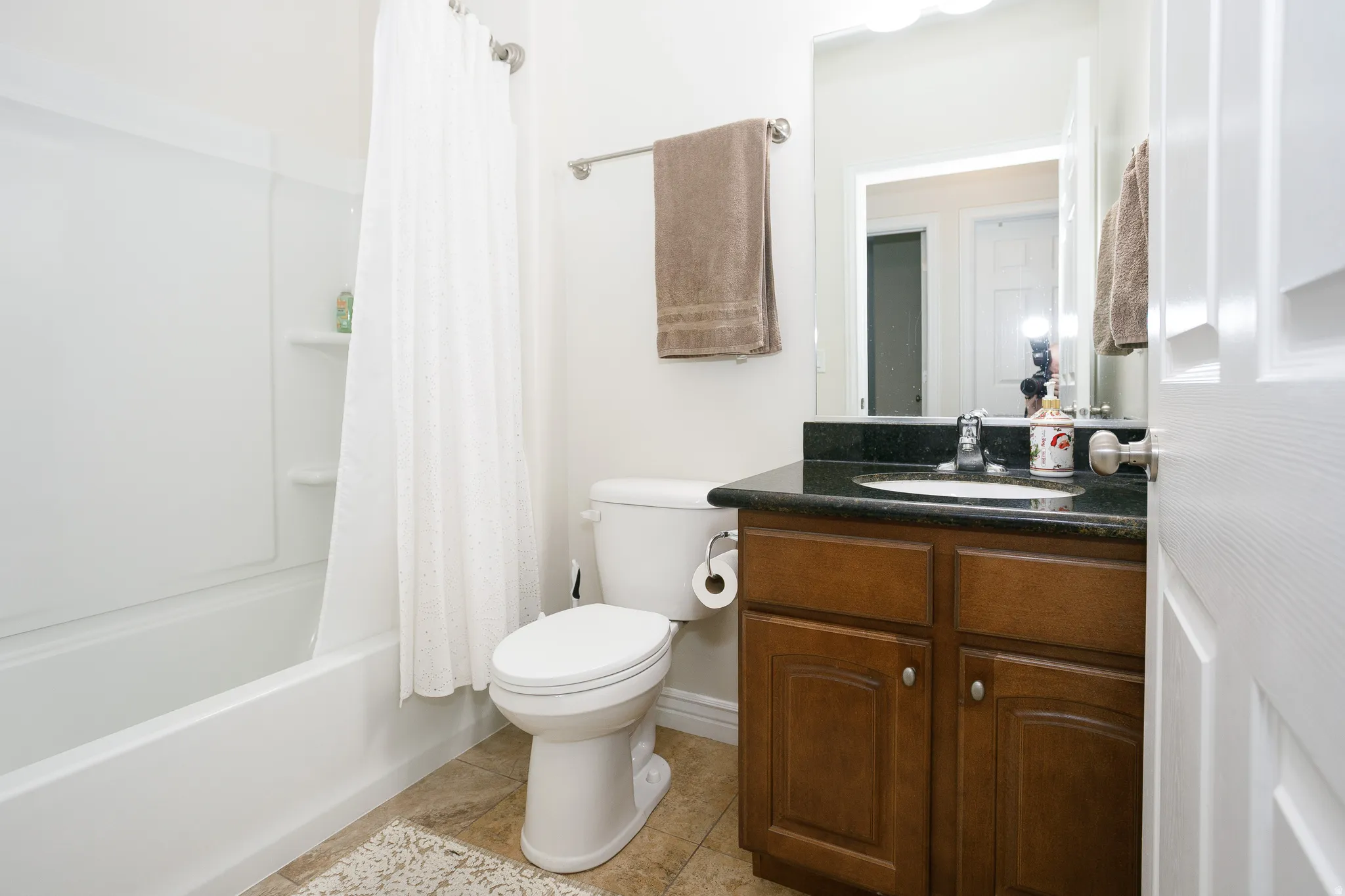 White bathtub with integrated shelving, dark wood-finish vanity with a dark countertop, and a built-in mirror
