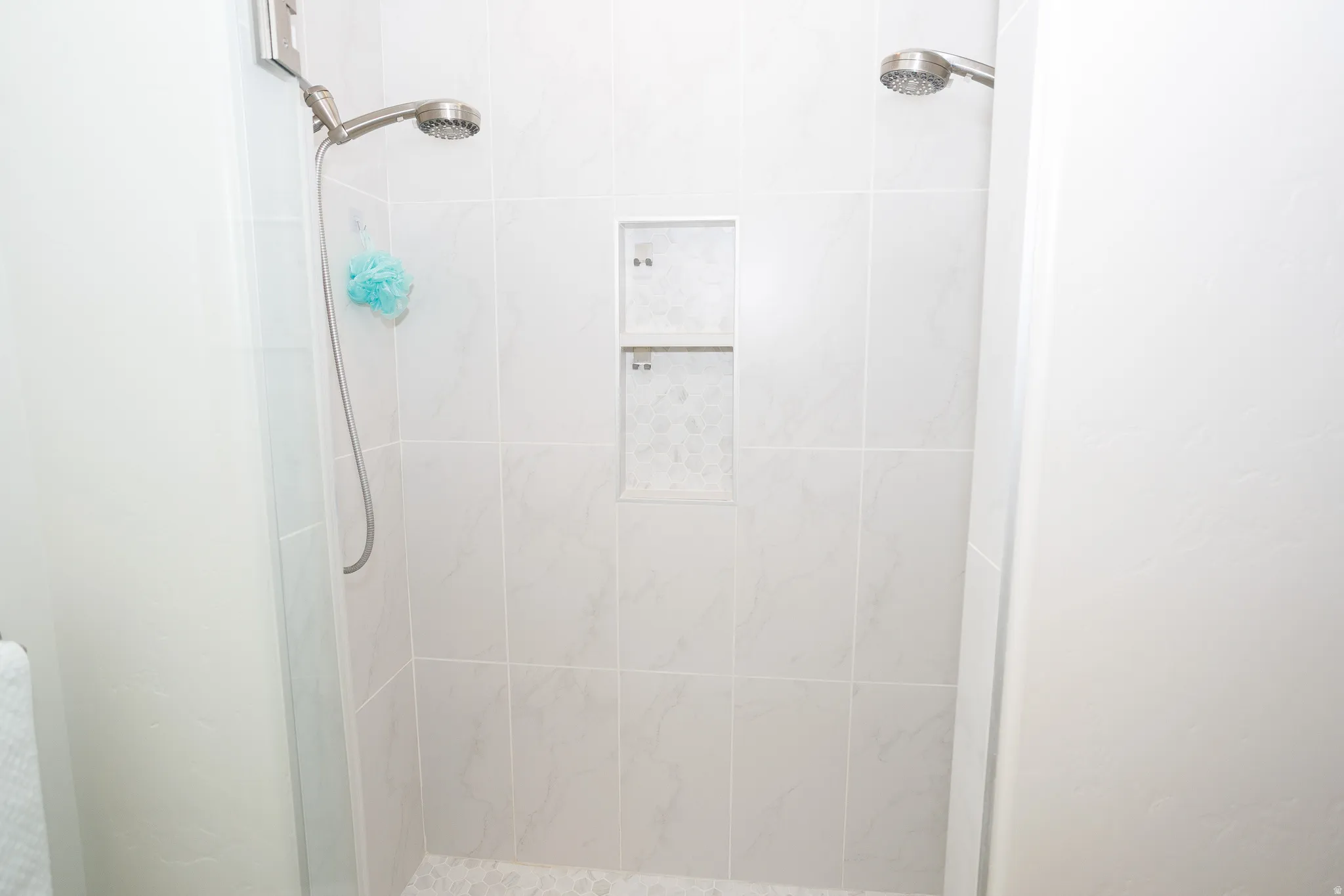 Dual shower heads, tiled shower walls, built-in shower niche, and tiled shower floor