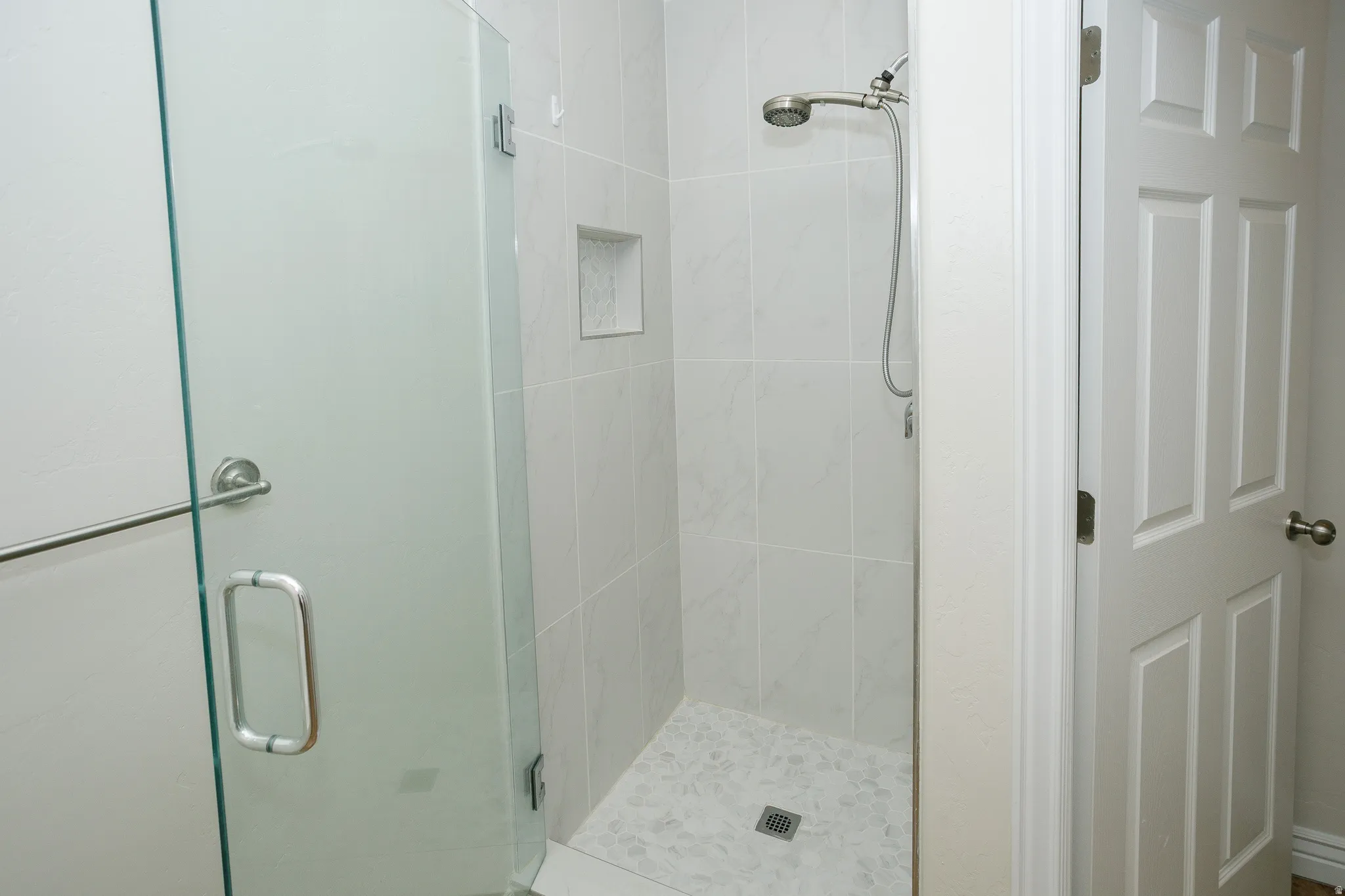 Shower with frameless glass enclosure, tiled walls, and a built-in niche
