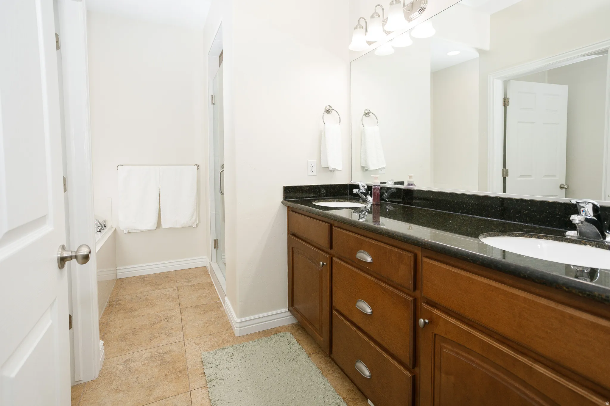 Dual vanity with dark stone countertop, wood-finish cabinetry, and chrome fixtures