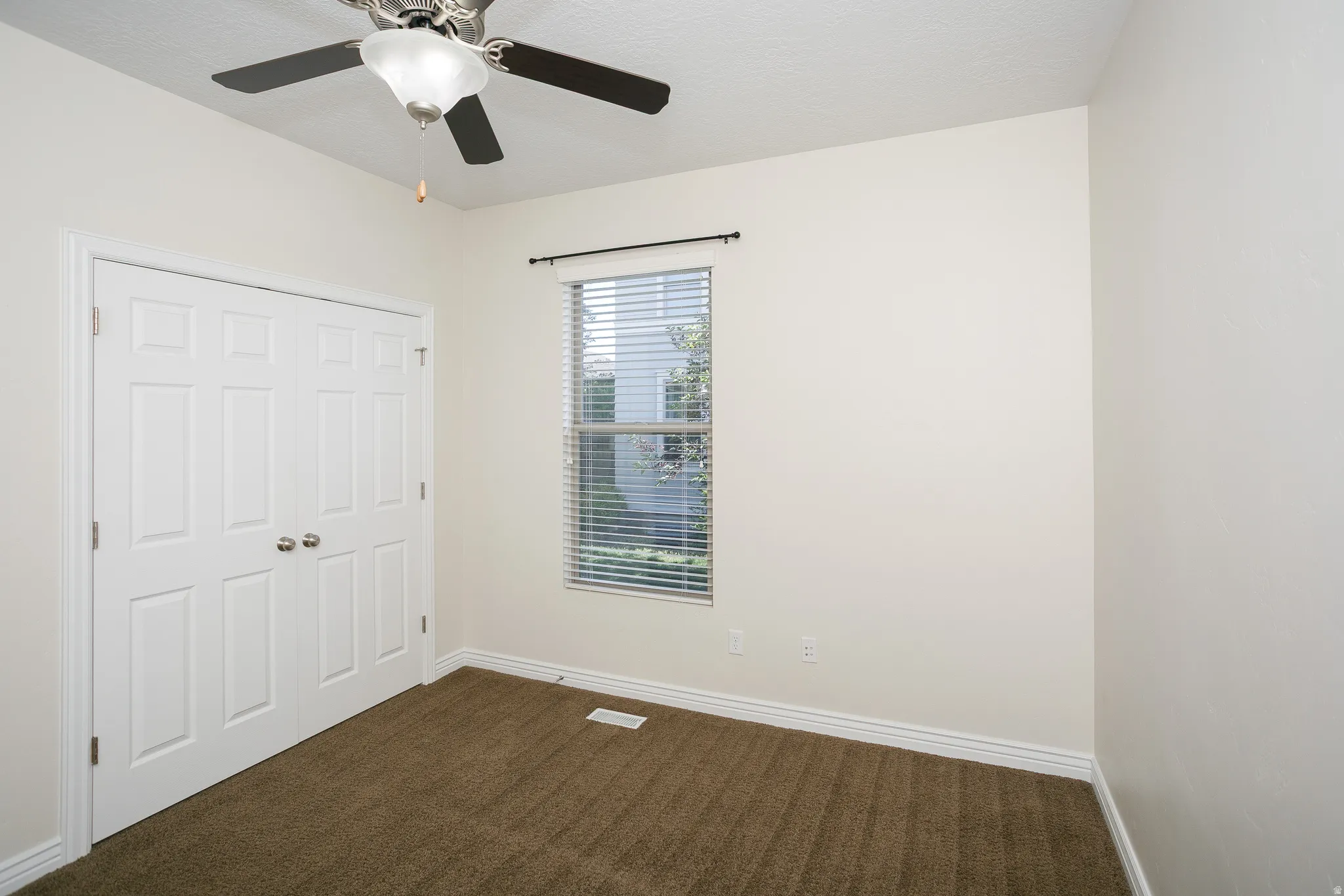Ceiling fan with integrated lighting, window with blinds, dual paneled closet doors, and neutral carpeting