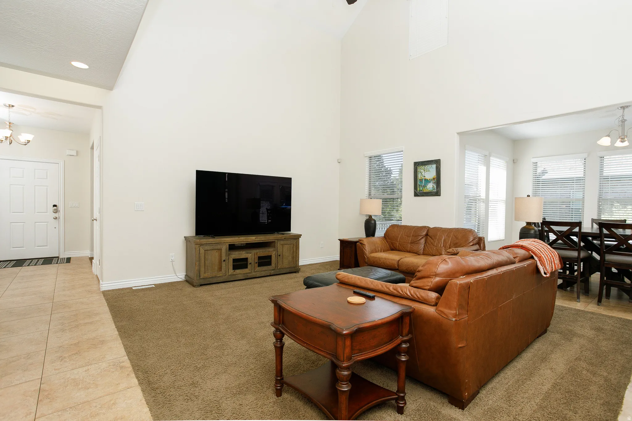 Vaulted ceiling with recessed lighting, large windows with horizontal blinds, carpeted flooring, and a tiled entry