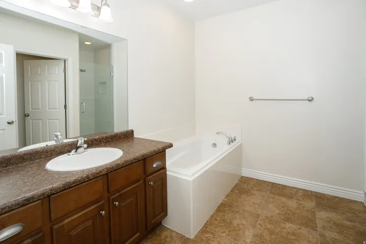 Spacious bathroom featuring a built-in soaking tub, a vanity with a drop-in sink, a large wall-mounted mirror, and tile flooring