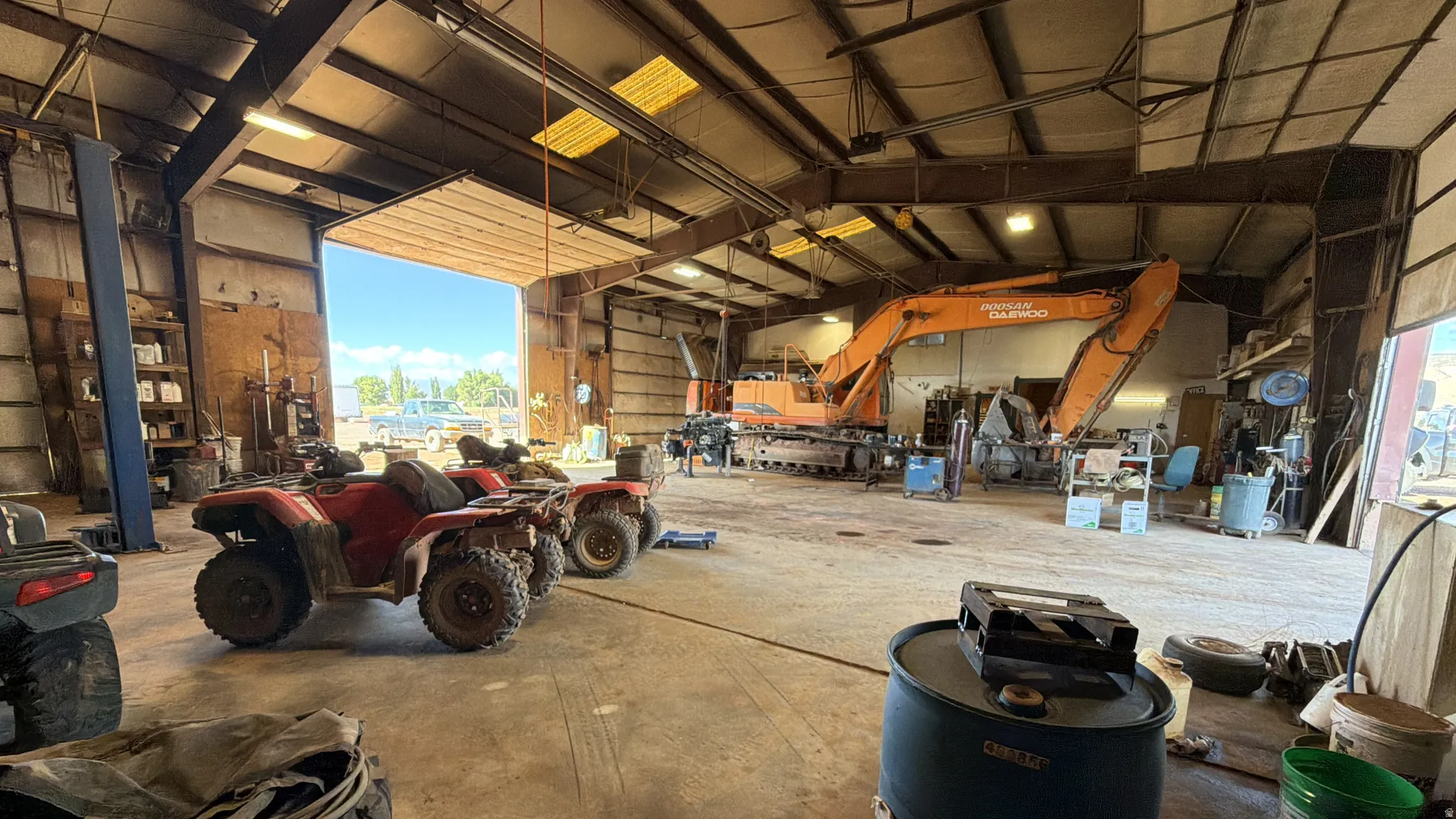 Spacious industrial interior with high ceilings, exposed structural beams, concrete flooring, and a large roll-up door