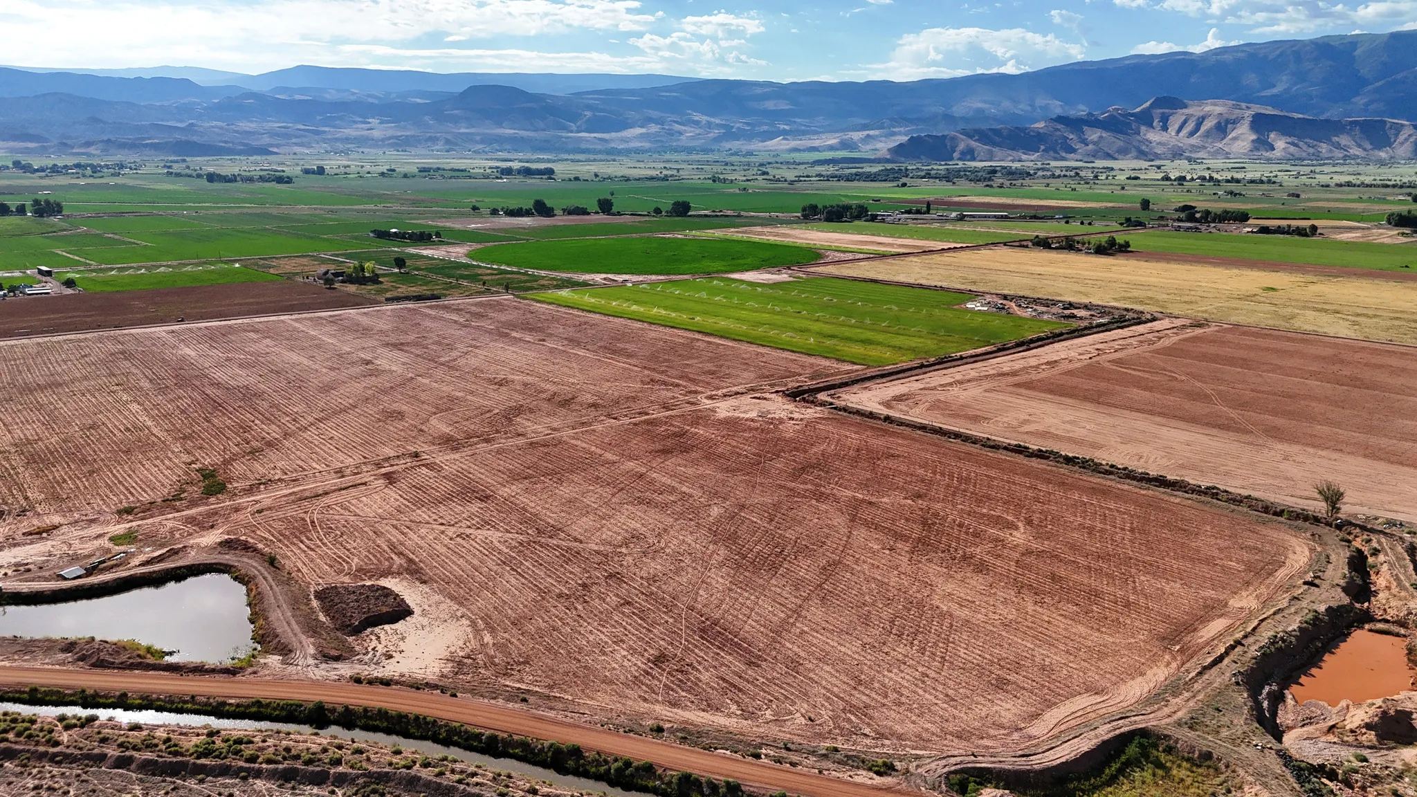 Expansive agricultural property featuring multiple tilled fields, established irrigation channels, natural water features, and distant mountain backdrops
