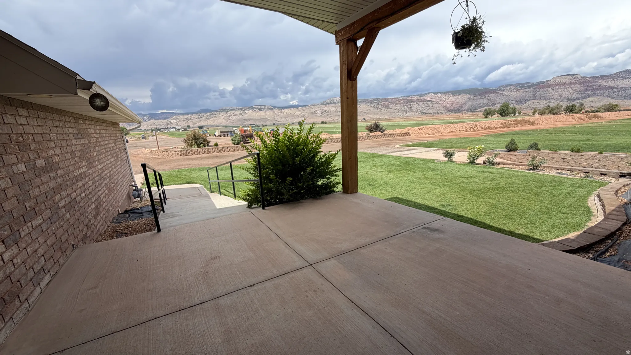 Expansive concrete patio with a covered outdoor area, offering distant mountain scenery and a manicured lawn
