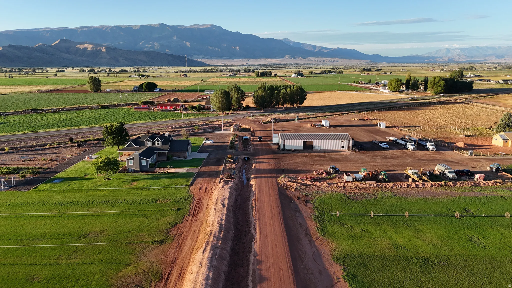 Expansive property featuring a modern residence with a dark roof, a large agricultural building, and surrounding fields