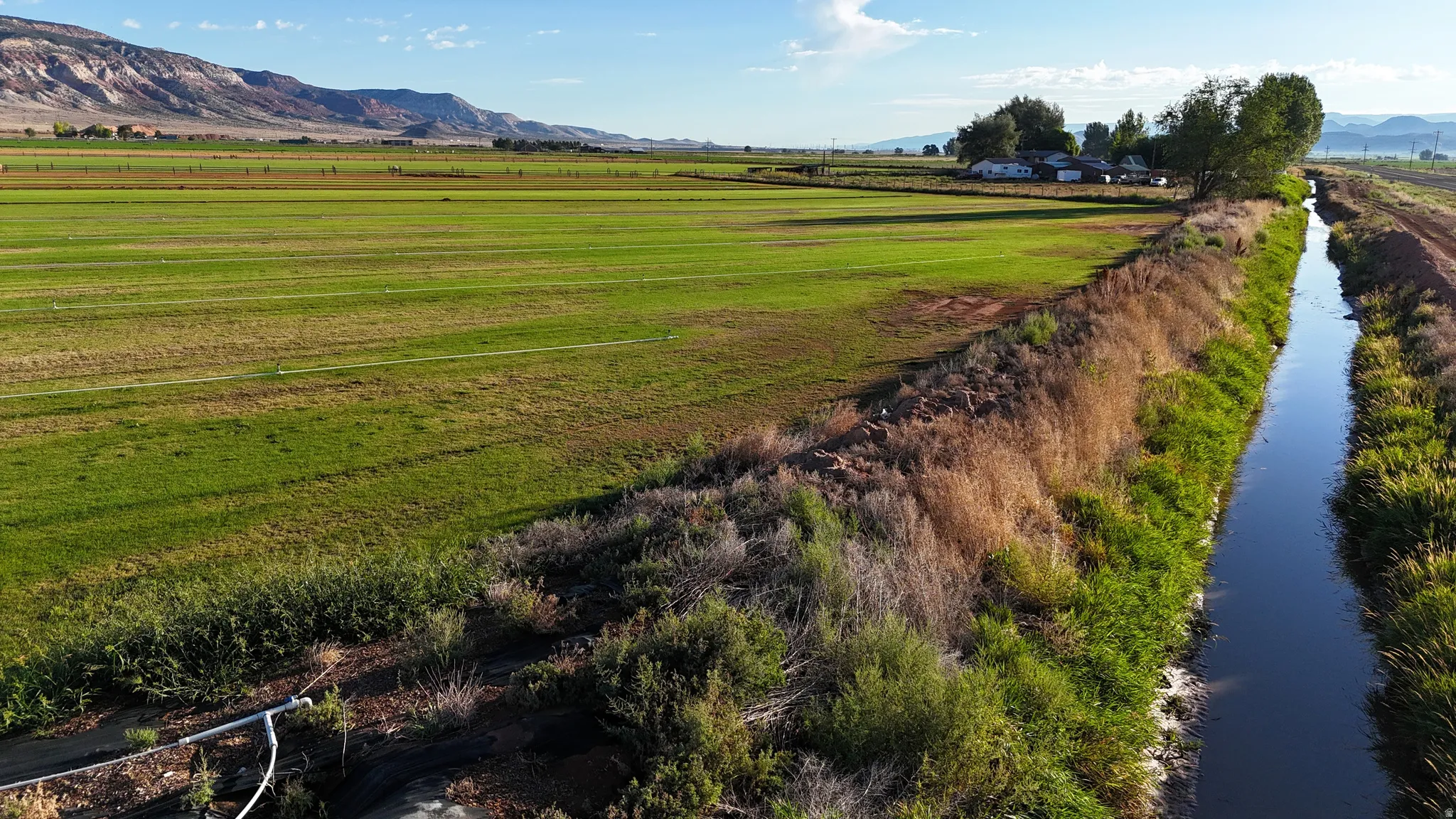 Expansive agricultural fields with irrigation infrastructure, bordered by a waterway and distant mountains