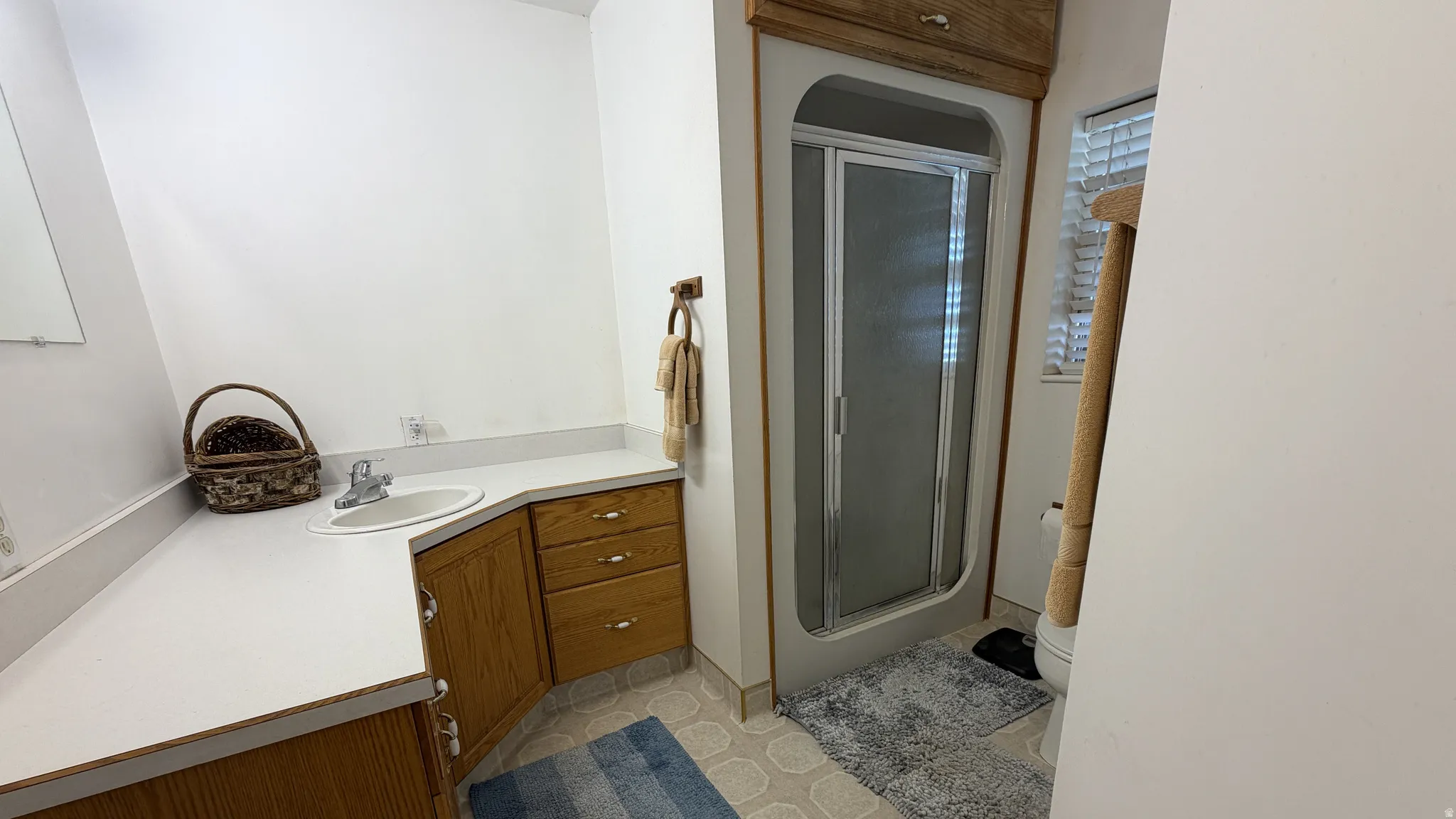 Built-in vanity with a corner sink, light wood cabinetry, and white countertops