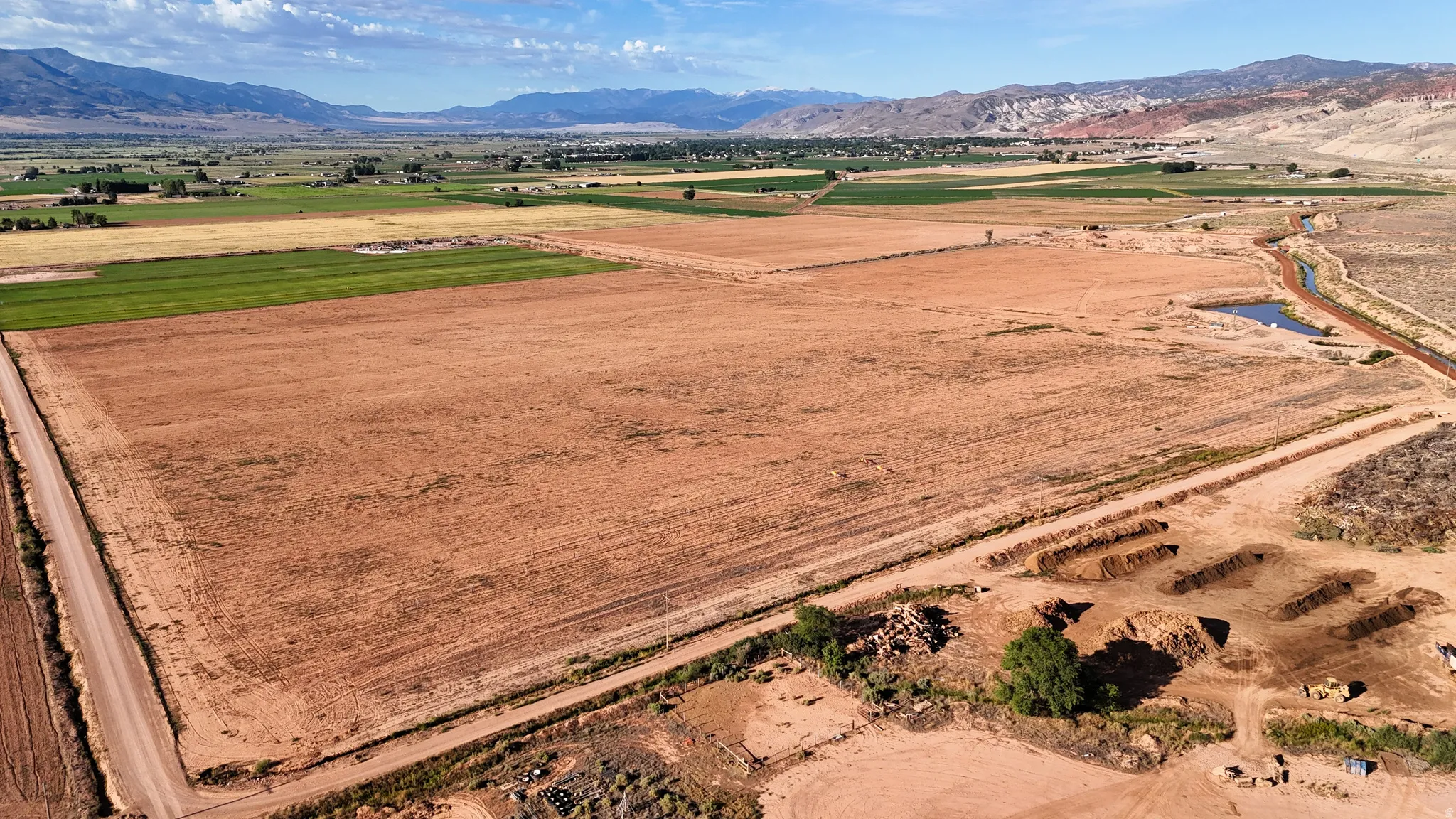 Expansive land parcel featuring open fields, a natural water body, and a distant mountain range