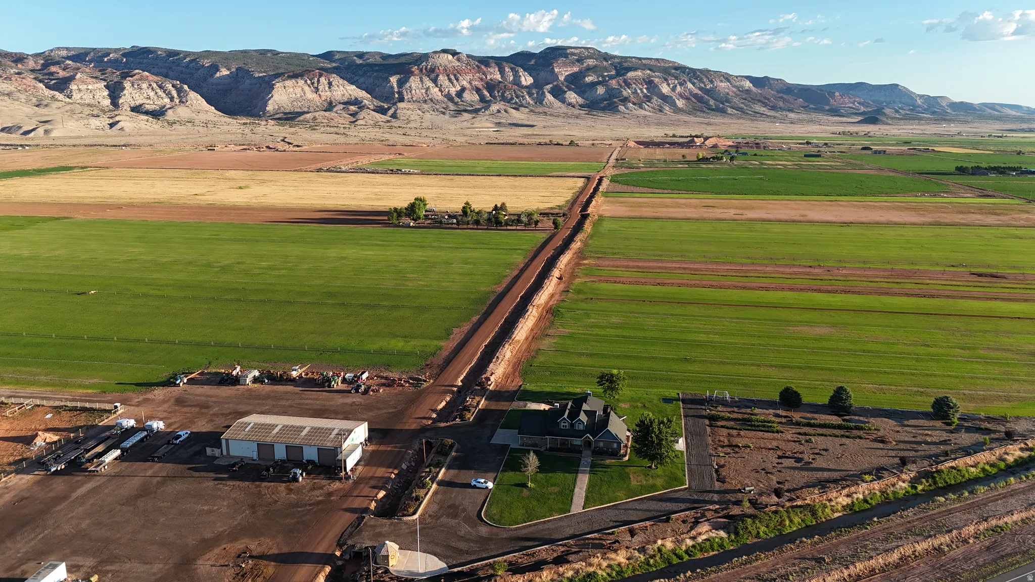Expansive agricultural lands with distant mountain formations, a paved driveway, and a large outbuilding
