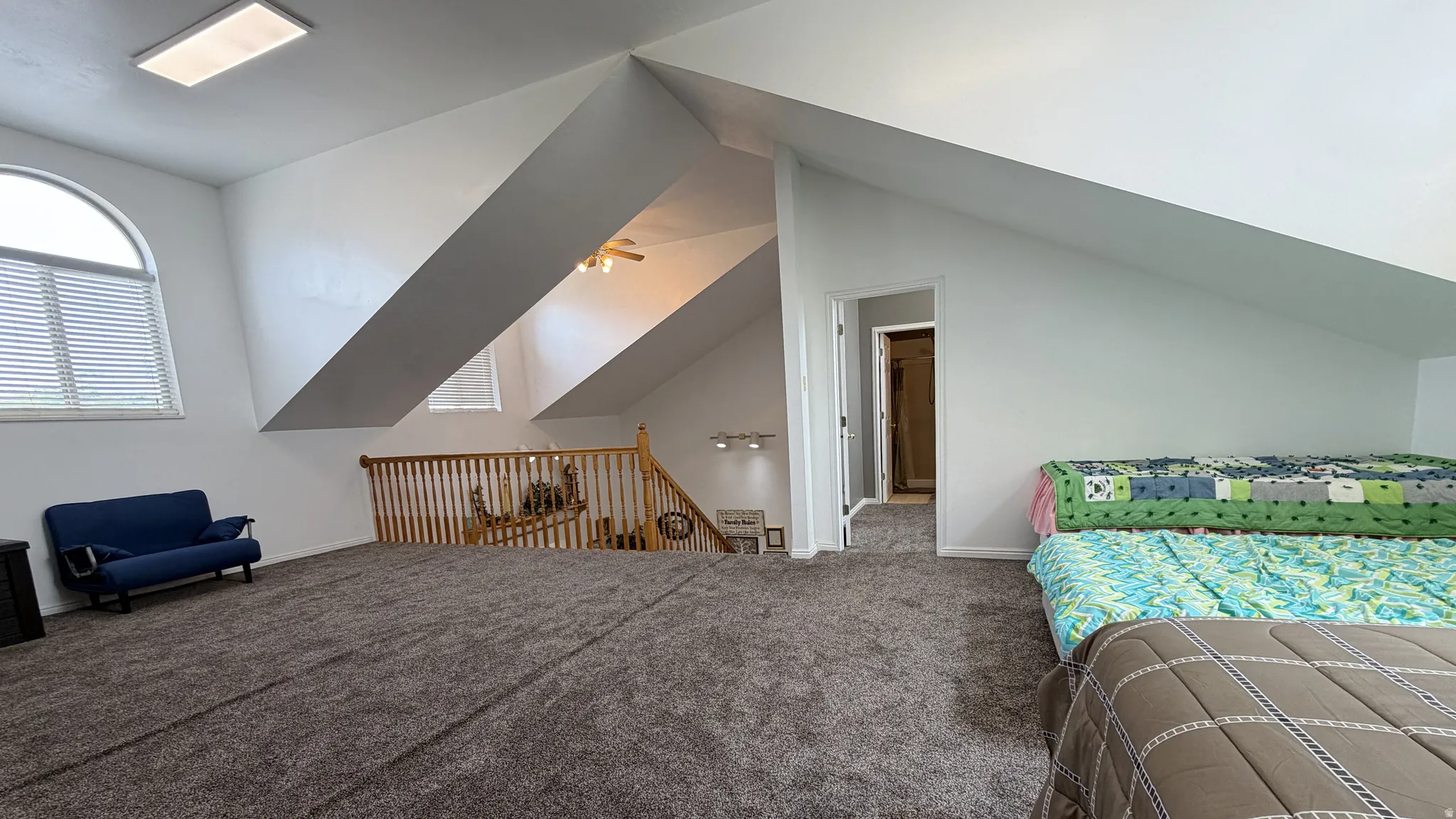 Carpeted loft space featuring an arched window with blinds, a wooden railing, a rectangular ceiling light fixture, and an interior doorway